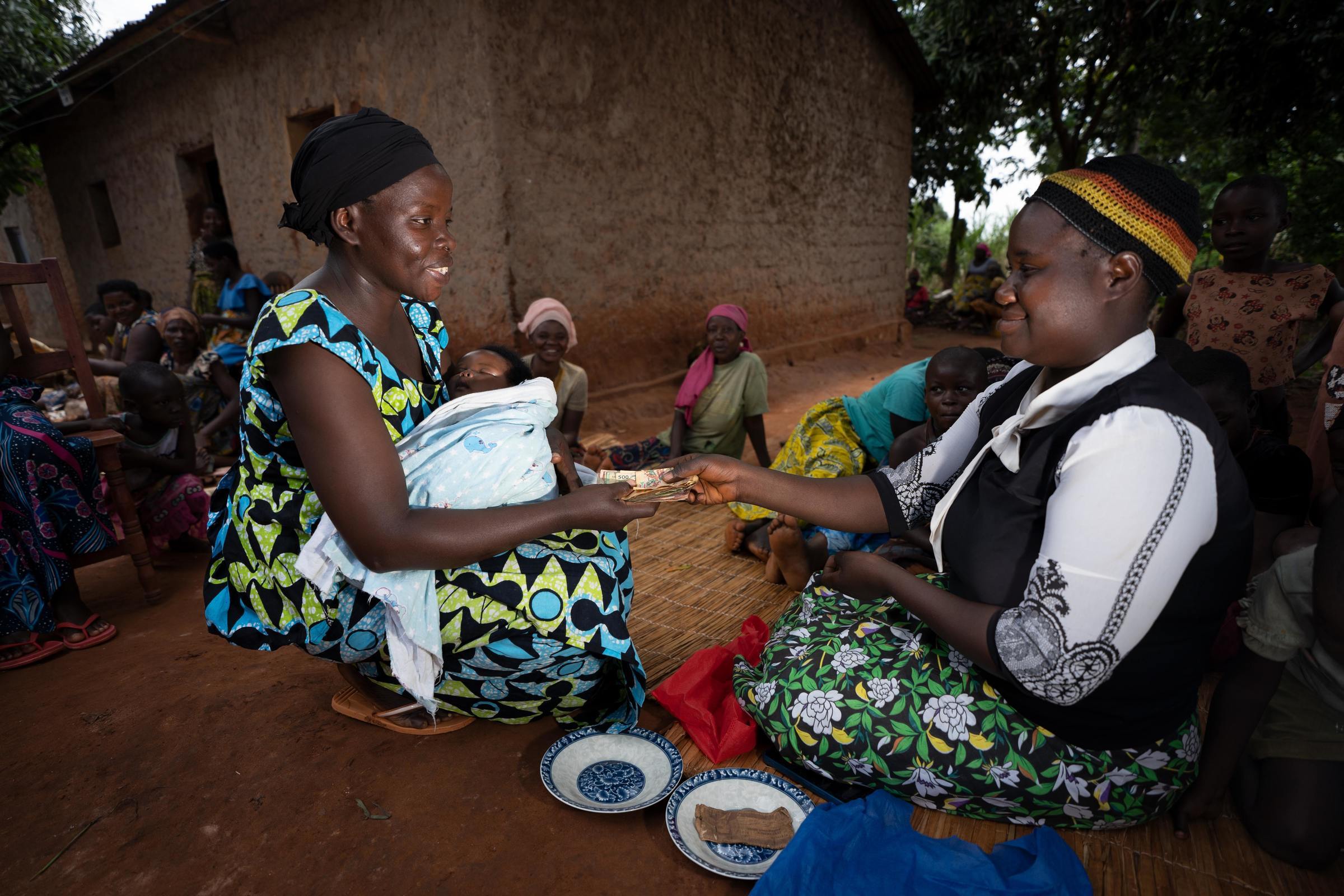 Two women of a self-help group sit on the floor. One turns a bundle of money over to the other (Quelle: Christian Nusch)