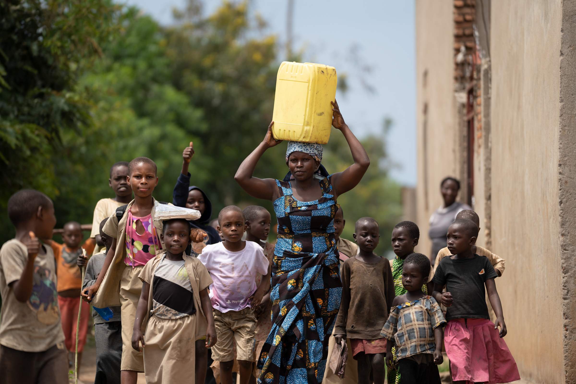 A women with a water canister on her head walks in a group of children (Source: Christian Nusch)