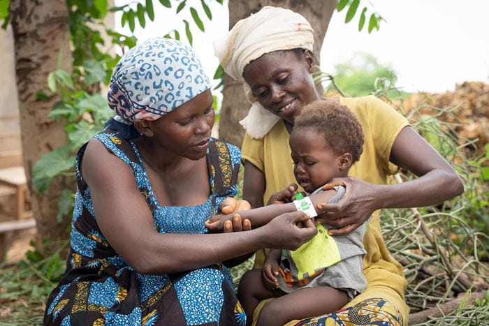 A health assistant measures the arm size of a baby who sits on the lap of the mother (Source: Christian Nusch)