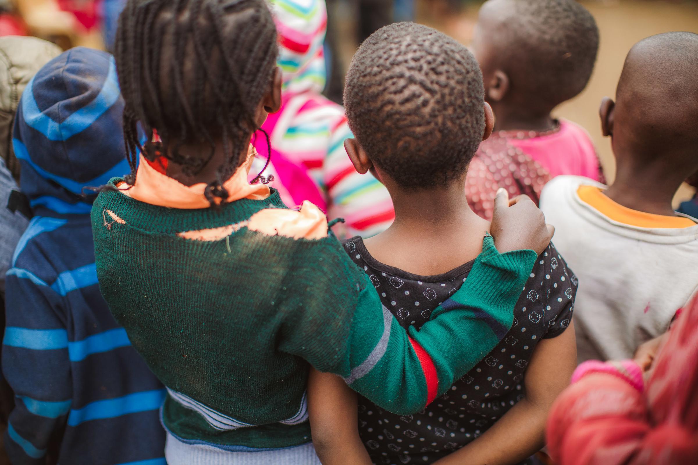 A group of childre from behind. One girl has put her arm around another. Her shirt is torn (source: Lars Heidrich)