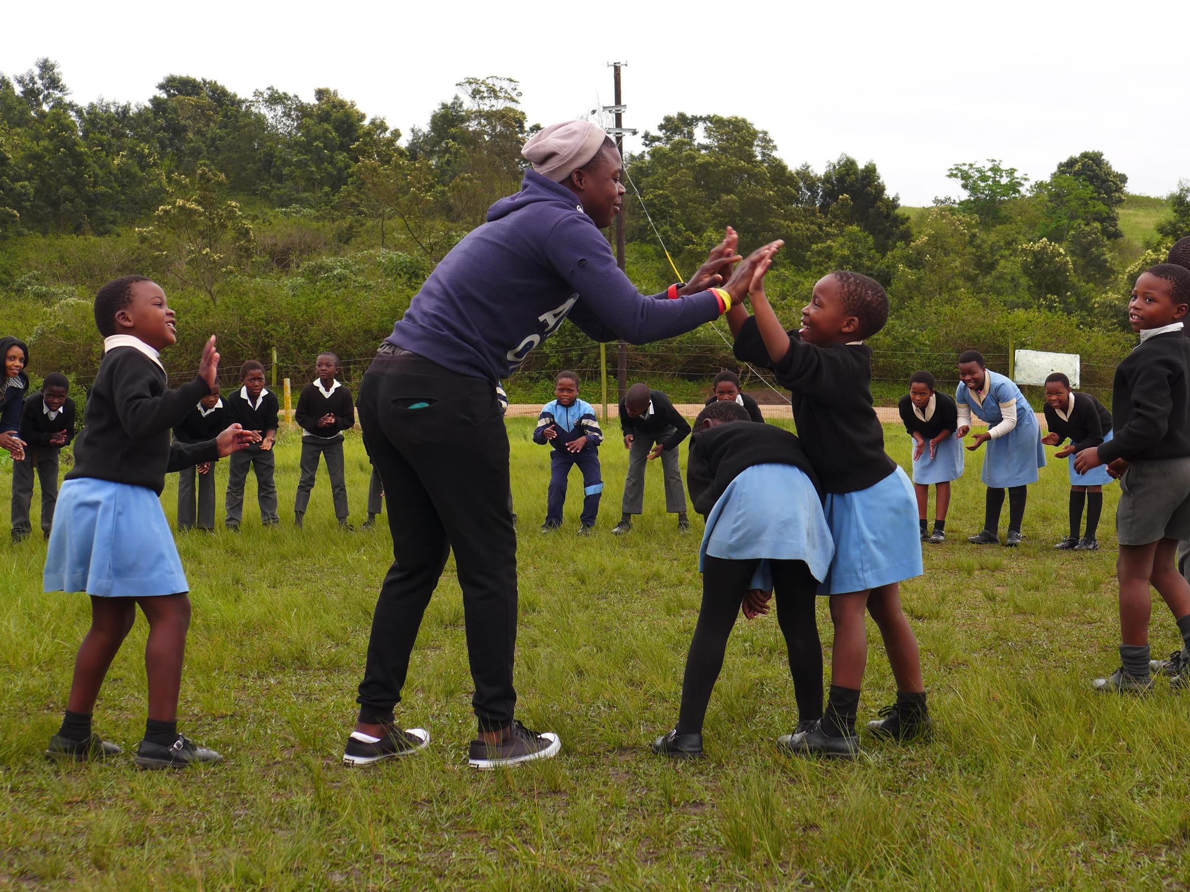 Children play in a circle outside a clapping game with a care giver (source: Niklas Alof)